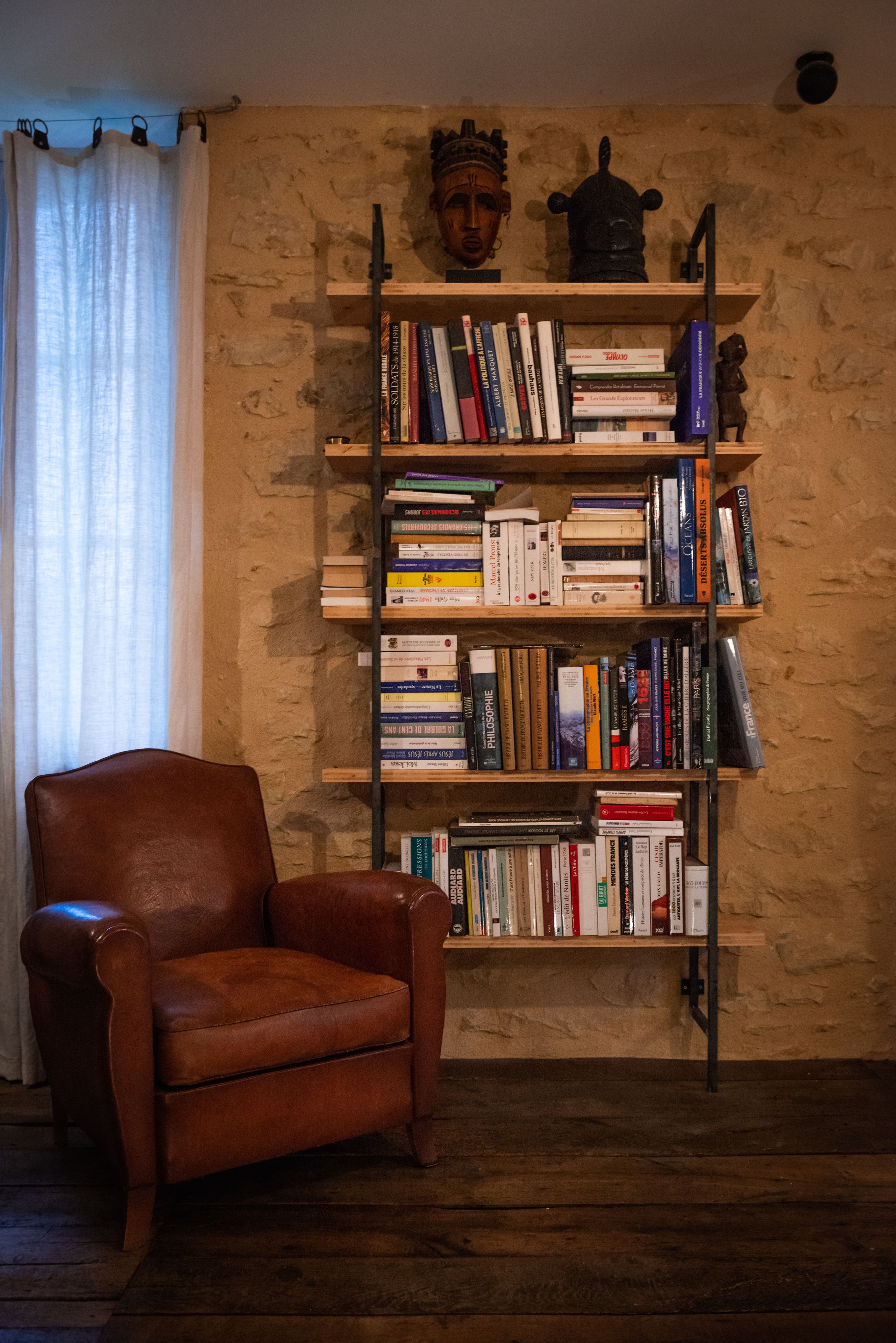 A room with a leather armchair, a bookshelf filled with books, and a stone wall.