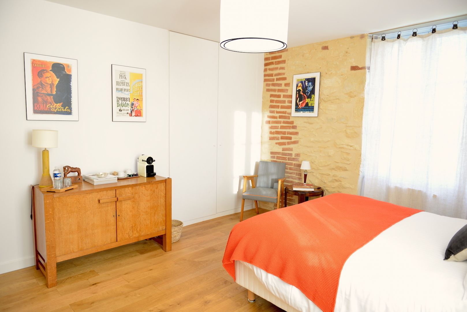 A bedroom with a bed, a wooden dresser, a chair, and two posters on the wall.