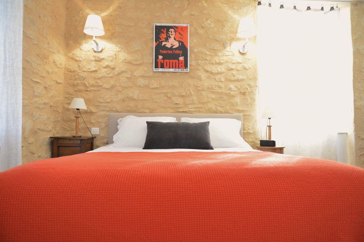 Ein Schlafzimmer mit einer Steinsturz, einem Bett mit weißer und schwarzer Bettwäsche, zwei Nachttischlampen und einem Poster an der Wand.