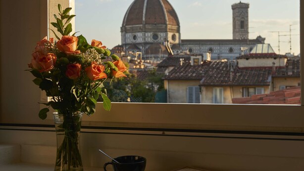 Une fenêtre avec un vase de fleurs, une tasse et un livre posés sur le rebord de la fenêtre.