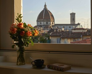 Una ventana con un jarrón de flores, una taza y un libro en el alféizar.