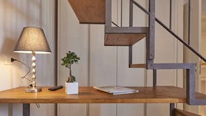 Un escalier moderne avec des marches en bois et des rampes en métal, un bureau en bois avec une lampe, une petite plante et une télécommande.