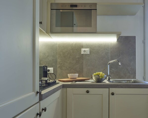 A modern kitchen with a built-in oven, a kettle, a bowl of fruit, and a cutting board. - Panoramic Suites Cavour 34 (Florence)