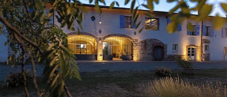 A building with arched windows and stone walls, surrounded by a gravel courtyard and some greenery.