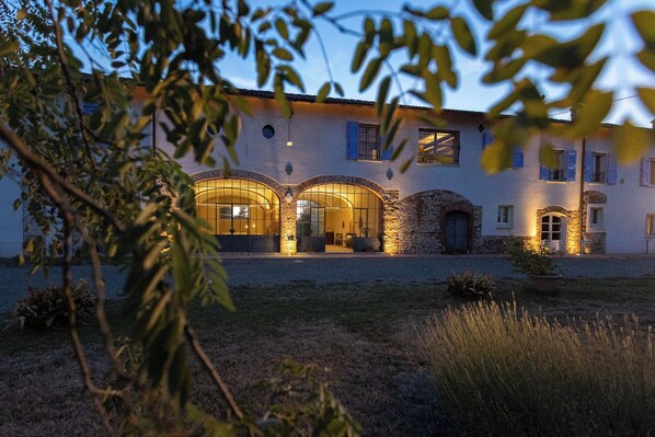 A building with arched windows and stone walls, surrounded by a gravel courtyard and some greenery.