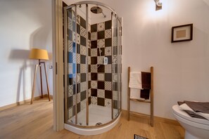 Una doccia con porta in vetro, pavimento in legno, portasci asciugamani e una lampada.