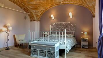 Une chambre avec un plafond en briques, un cadre de lit en métal blanc, une literie à motifs et une table de chevet avec des tiroirs.