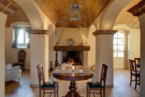 Una sala da pranzo con camino in mattoni, sedie di legno, un tavolo rotondo e una finestra con tende.