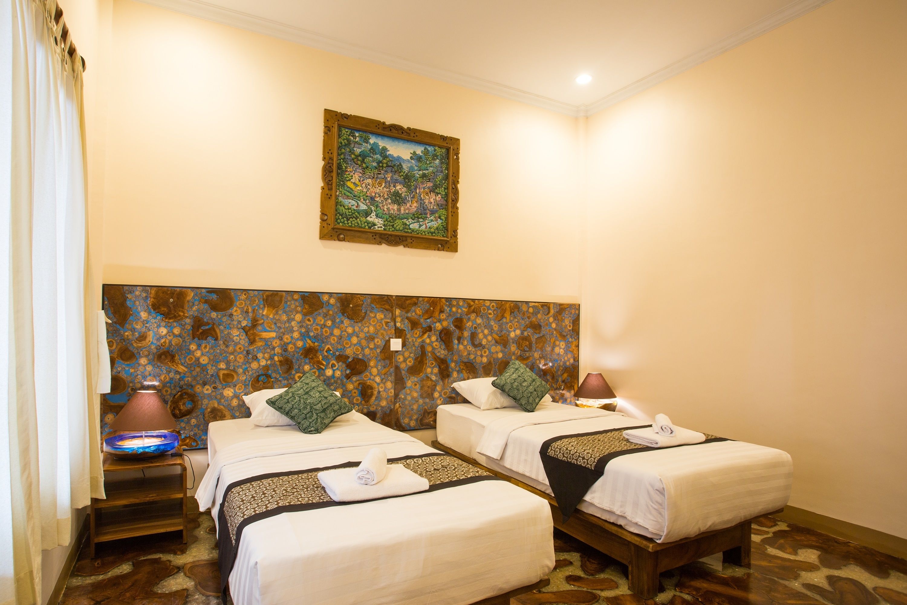 A hotel room with two beds, a nightstand with a lamp, a painting on the wall, and a patterned floor.