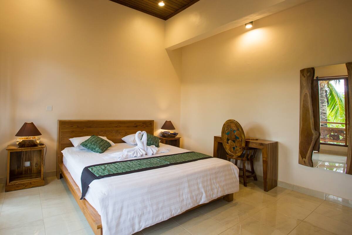 A spacious bedroom with a large bed, wooden headboard, and a wooden nightstand with a lamp.