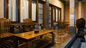 A traditional wooden dining area with high wooden tables and chairs, patterned window treatments, and a stone floor. - Bulan Bali Homestay (Ubud)