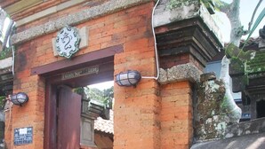 A traditional gate with a stone figure of a seated person, a red door, and a sign above the gate. - Bulan Bali Homestay (Ubud)