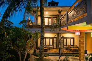 A two-story building with a balcony, a covered outdoor seating area, and a well-maintained garden.