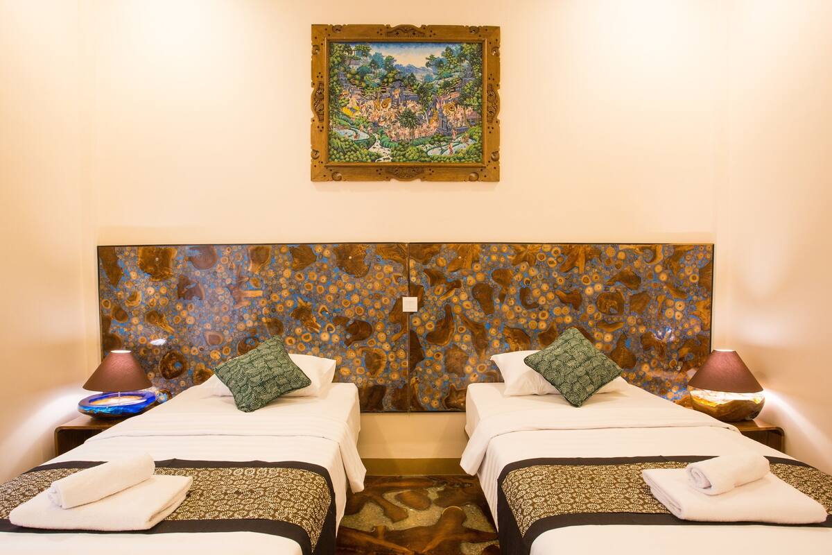 A hotel room with two beds, a large tapestry headboard, and a painting above the beds.