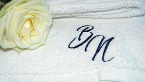 A white towel with embroidered initials and a white rose. - Bonne Nuit Guest House (Azzano San Paolo)