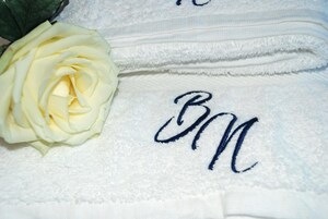 Un asciugamano bianco con ricamate iniziali e una rosa bianca.