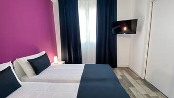 Una camera d'albergo con un letto, una TV a muro e una finestra con tende.