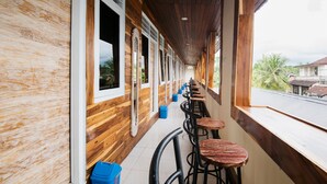 A covered outdoor seating area with wooden walls and windows, featuring a row of bar stools and blue trash bins. - Bulan Bali Guest House (Ubud)