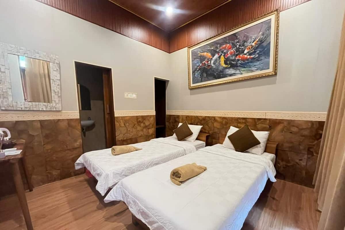 Quarto de hotel com duas camas, um quadro, um espelho e piso de madeira.