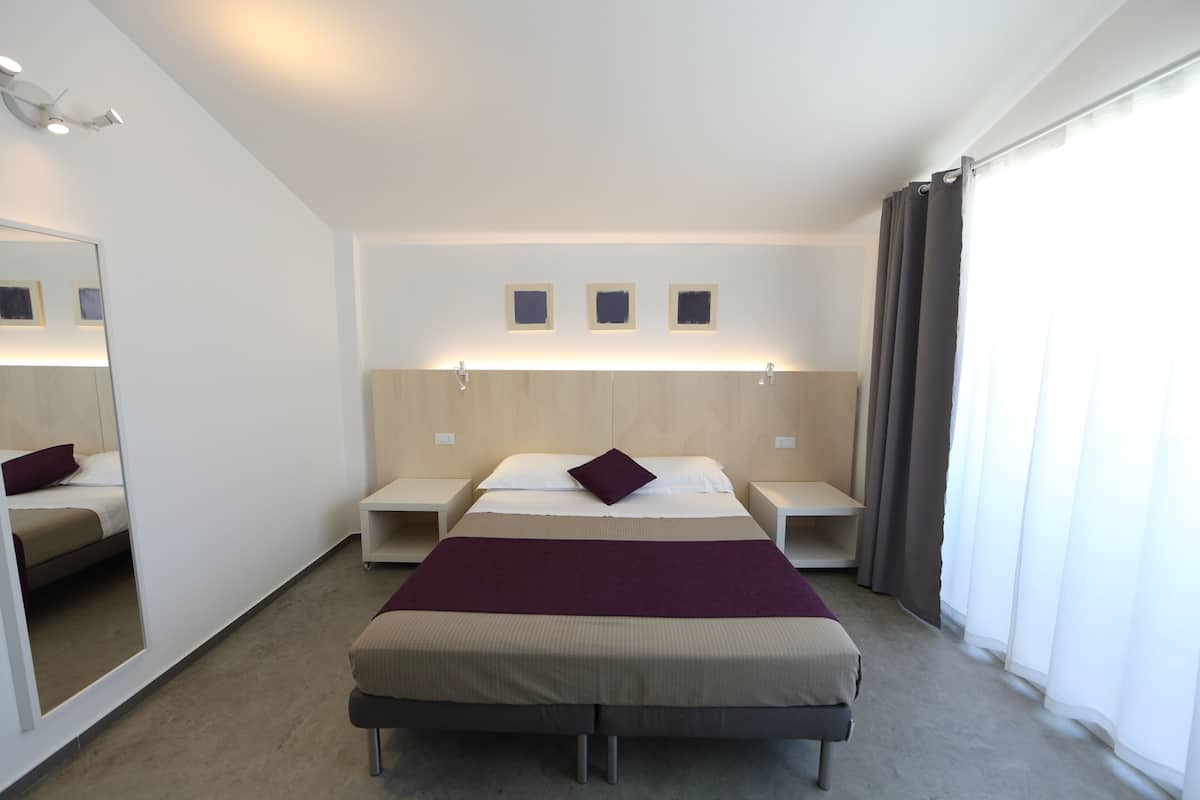 Habitación de hotel con una cama grande, mesitas de noche, un espejo y vistas al exterior.