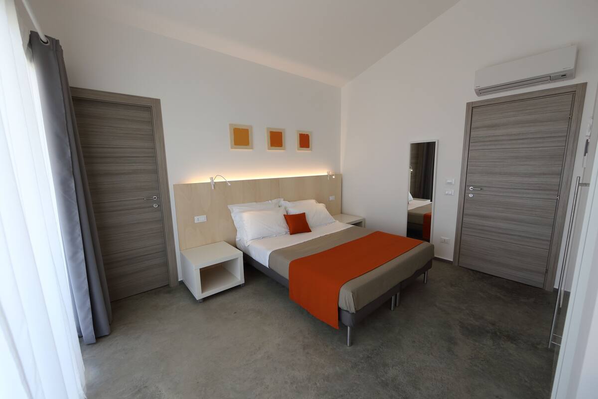Una habitación de hotel moderna con cama, mesitas de noche, un espejo y un armario.