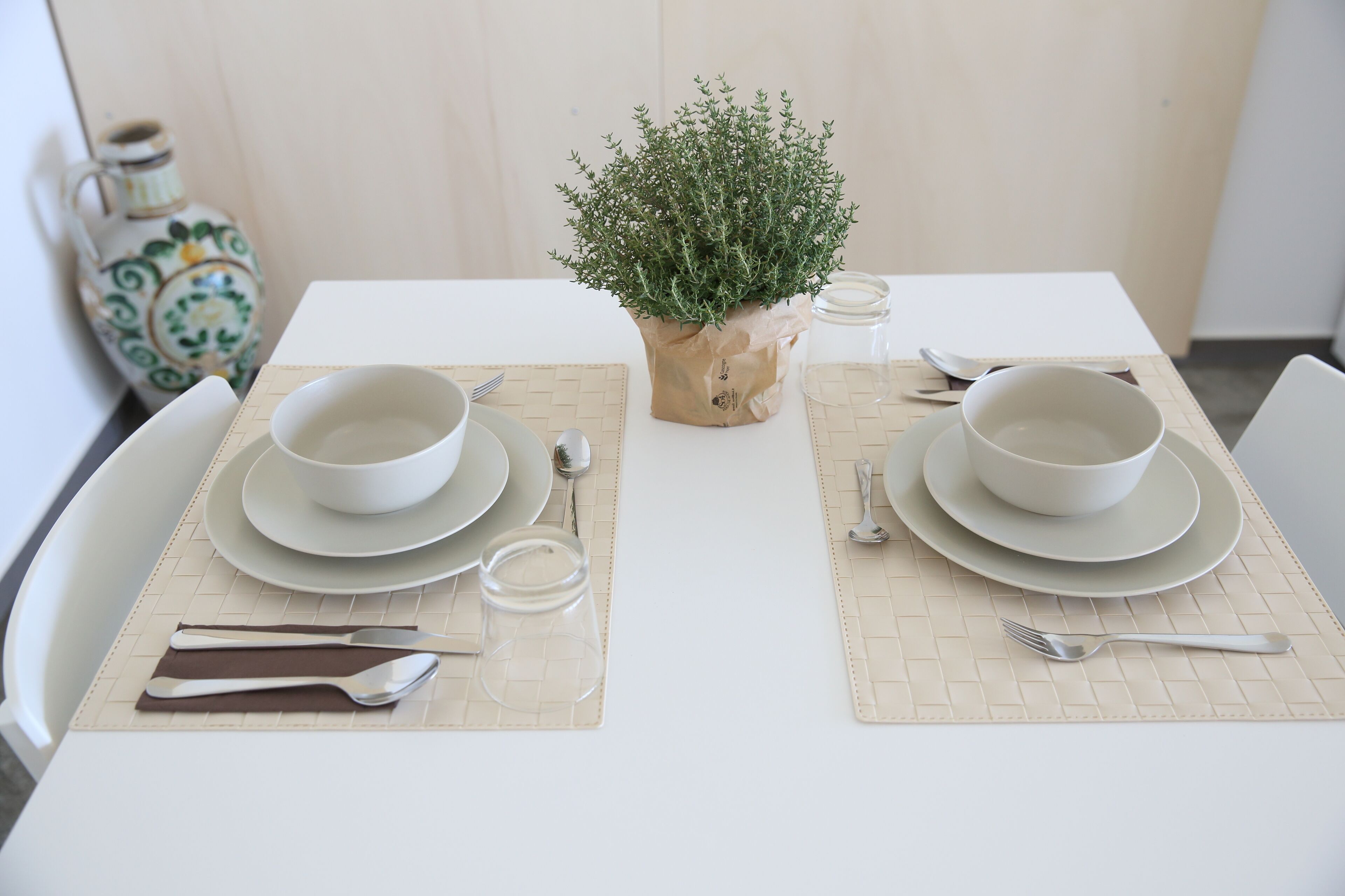 A neatly set dining table with two white plates, bowls, cutlery, and a small potted plant.