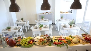 Un comedor con varias mesas dispuestas para comidas, cada una con sillas blancas, plantas en macetas y diversos alimentos.