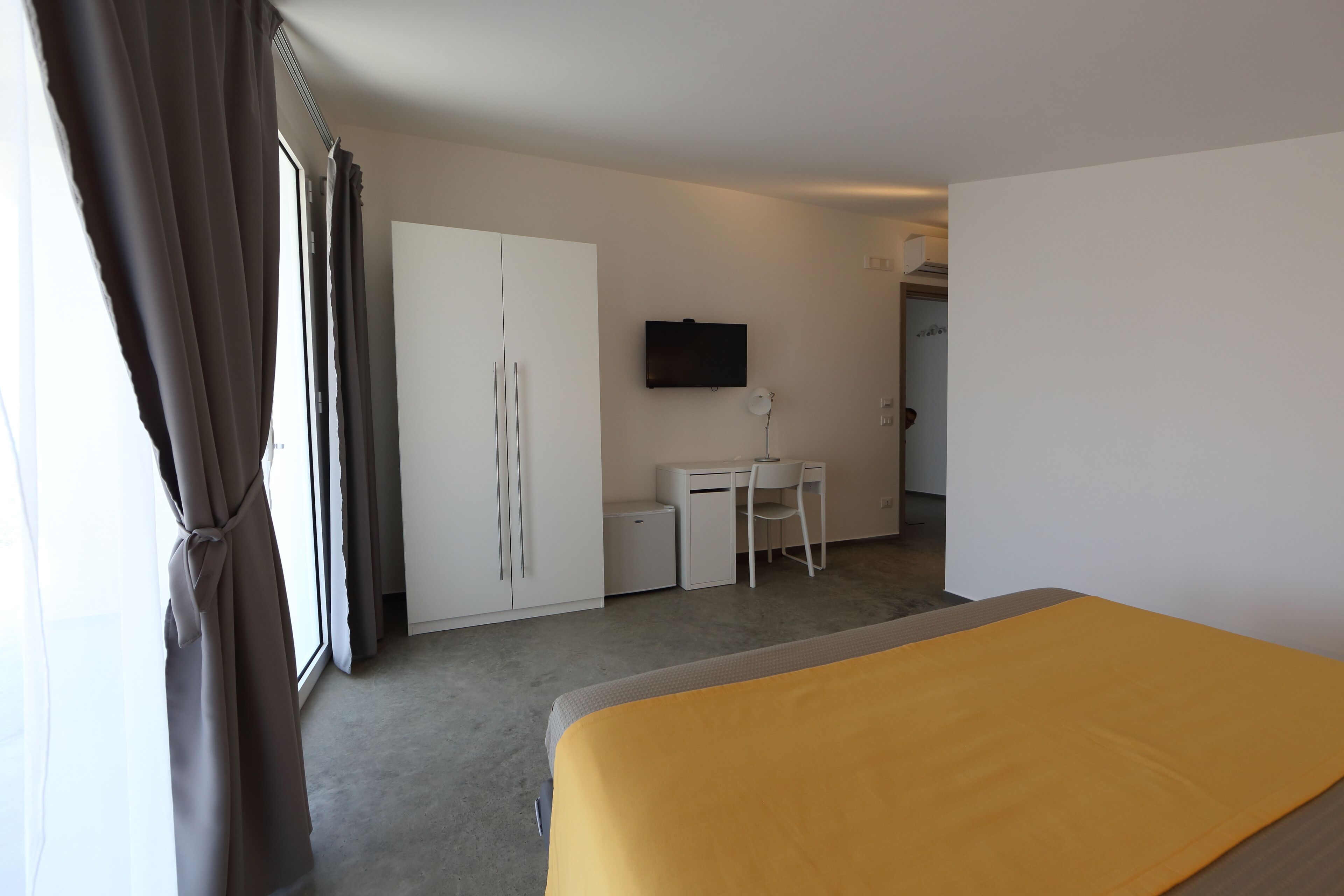 A hotel room with a bed, a desk, a chair, a TV, and a wardrobe.