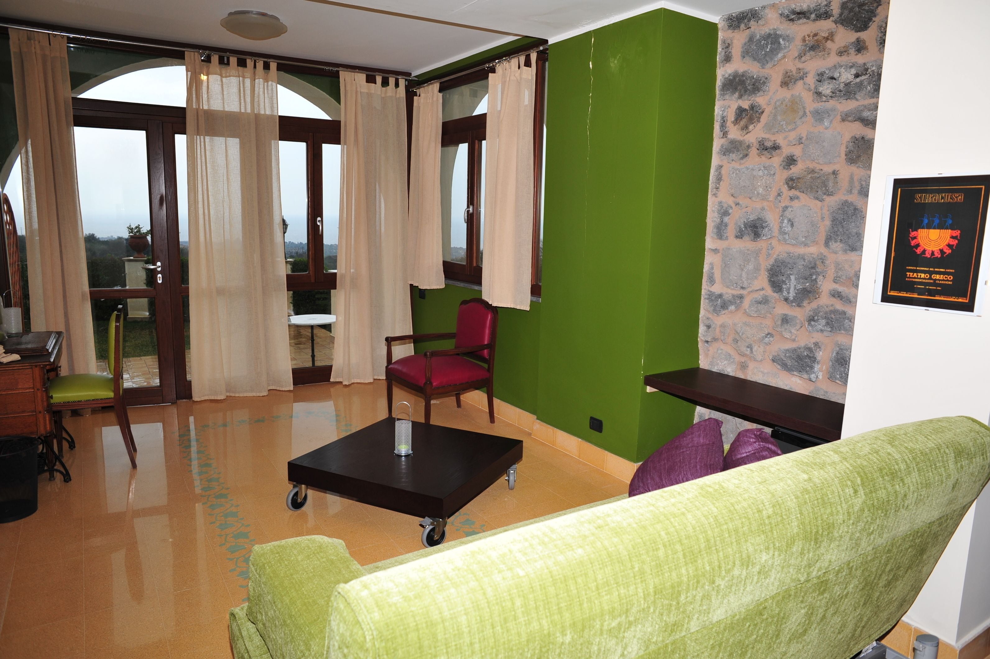 Una stanza con una parete verde, una parete decorata in pietra, un divano verde, una poltrona rossa, un tavolino e vista panoramica da ampie finestre.