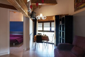 A room with a bed, a dining table with chairs, a sofa, and a TV on a wooden beam. - Tenuta Santa Tecla (Acireale)