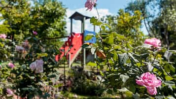 Stroll through a serene garden filled with blooming roses and a children's play area.