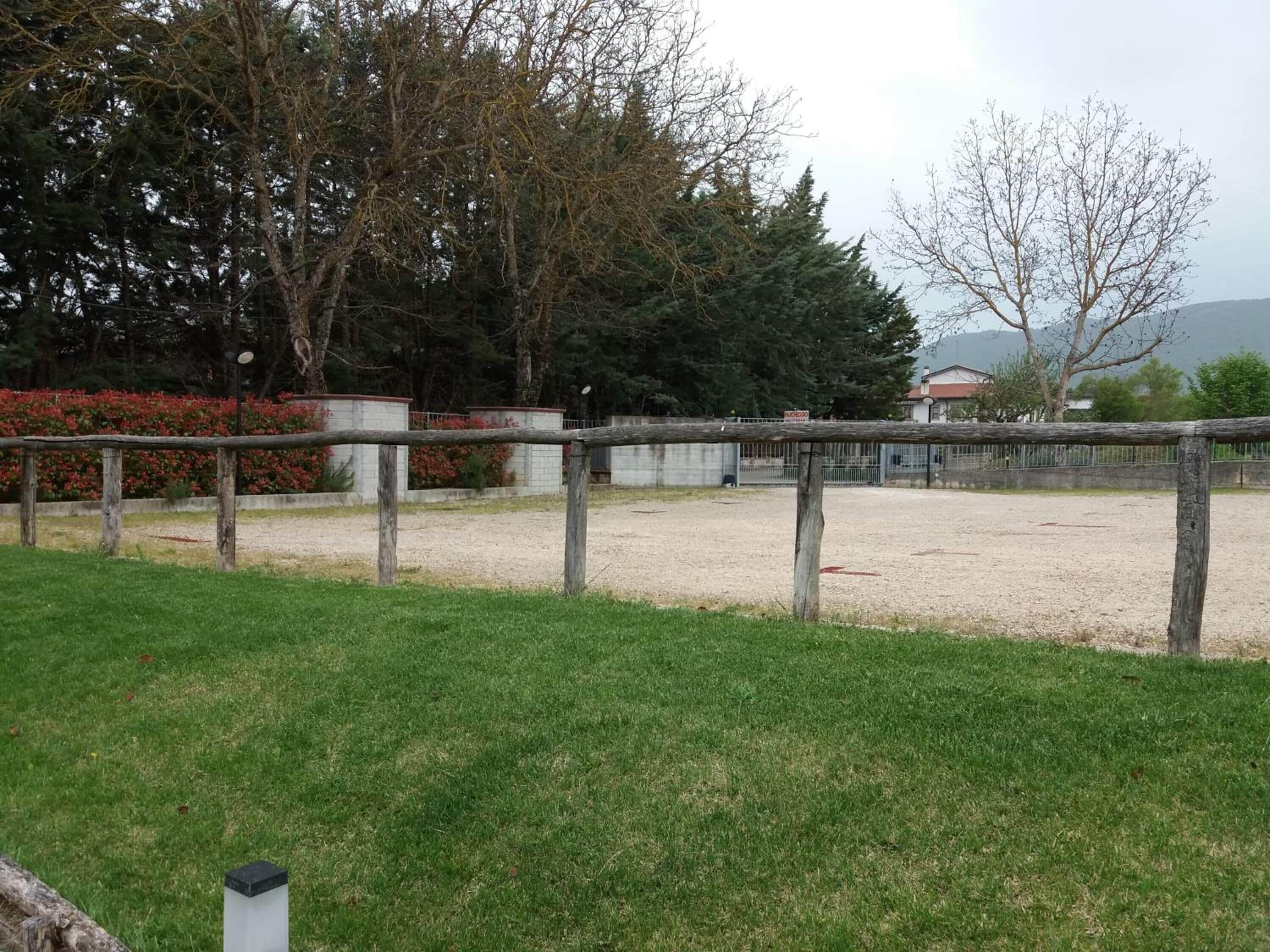 A fenced outdoor area with a gravel path, surrounded by grass and trees.