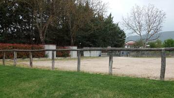 A fenced outdoor area with a gravel path, surrounded by grass and trees.