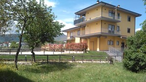 A yellow multi-story building with balconies, a grassy area in the foreground, and a tree to the left. - Affittacamere il Boscaiolo (L'Aquila)