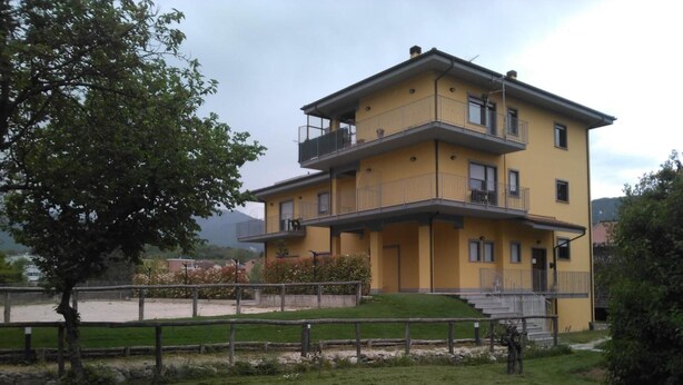 A two-story yellow building with a balcony on the upper floor, a small front porch, and a paved driveway. - Affittacamere il Boscaiolo (L'Aquila)