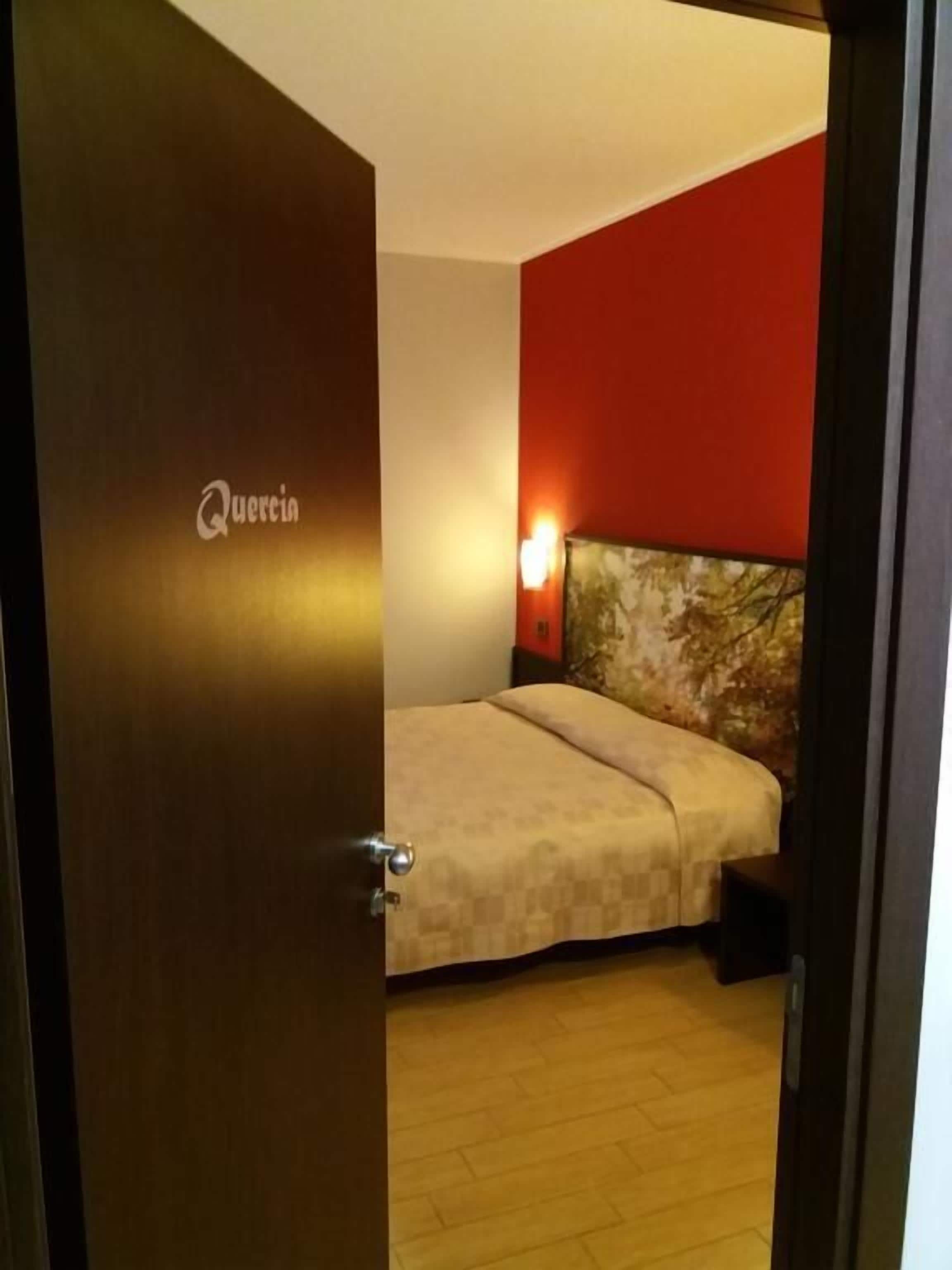 A hotel room with a bed, a nightstand, and a wall-mounted lamp.