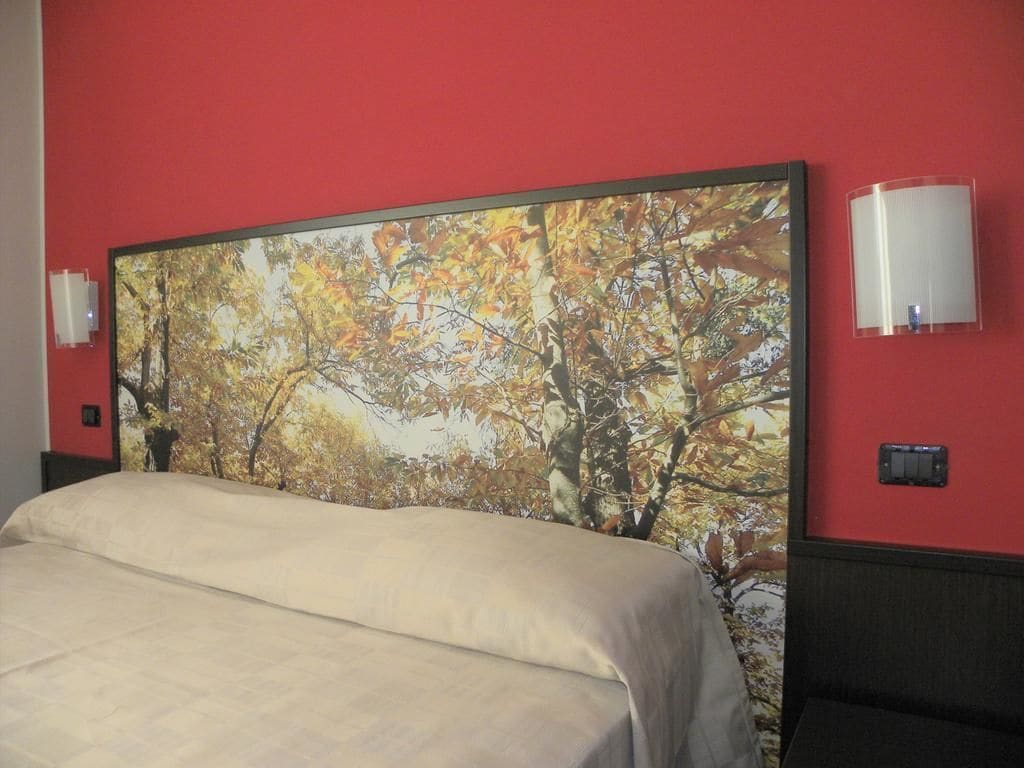 A hotel room with a large bed, a red wall, and a large painting of autumn leaves.