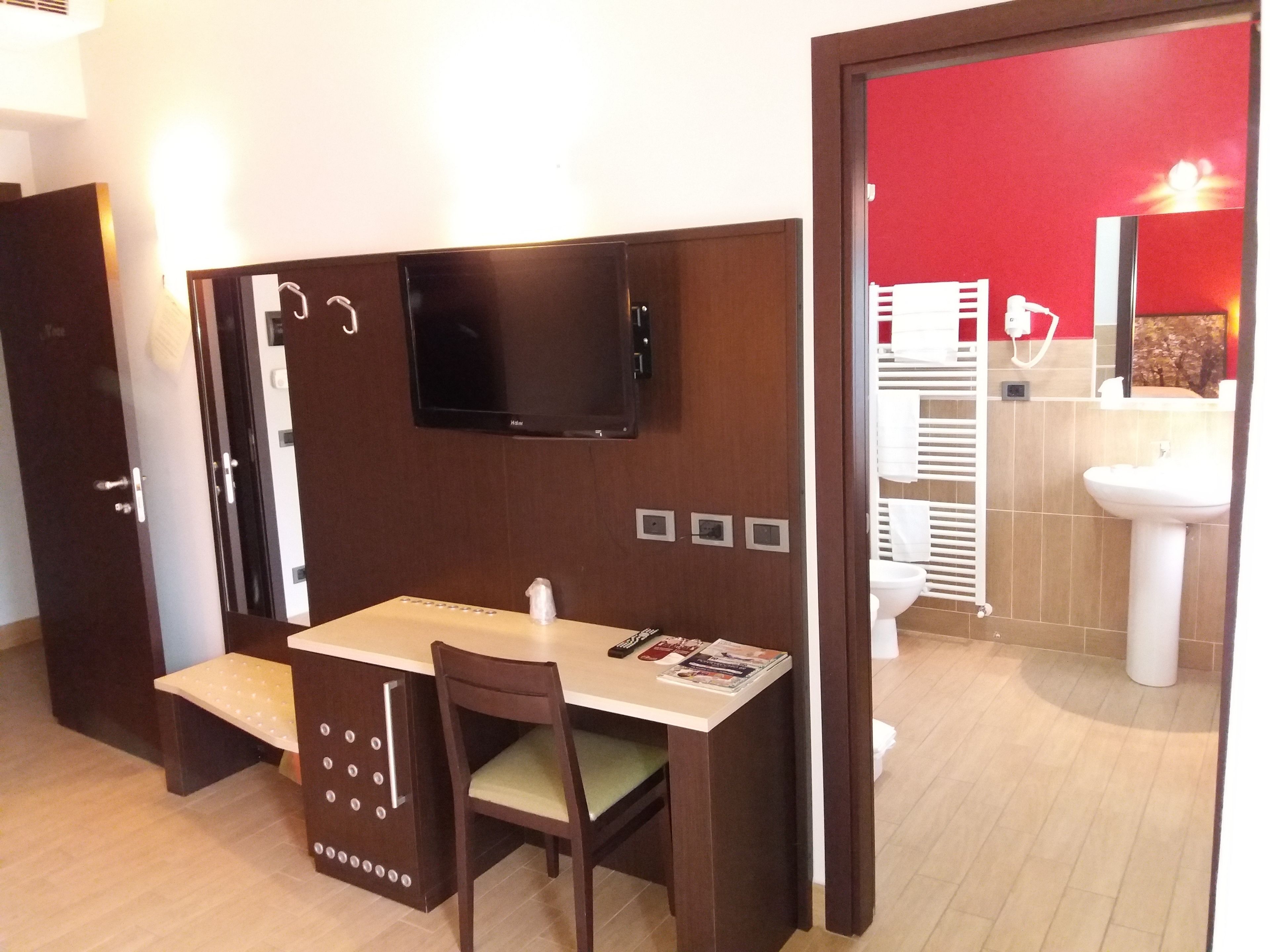 Ett kompakt hotellrum med ett skrivbord och en stol i trä, samt en väggmonterad platt-TV.