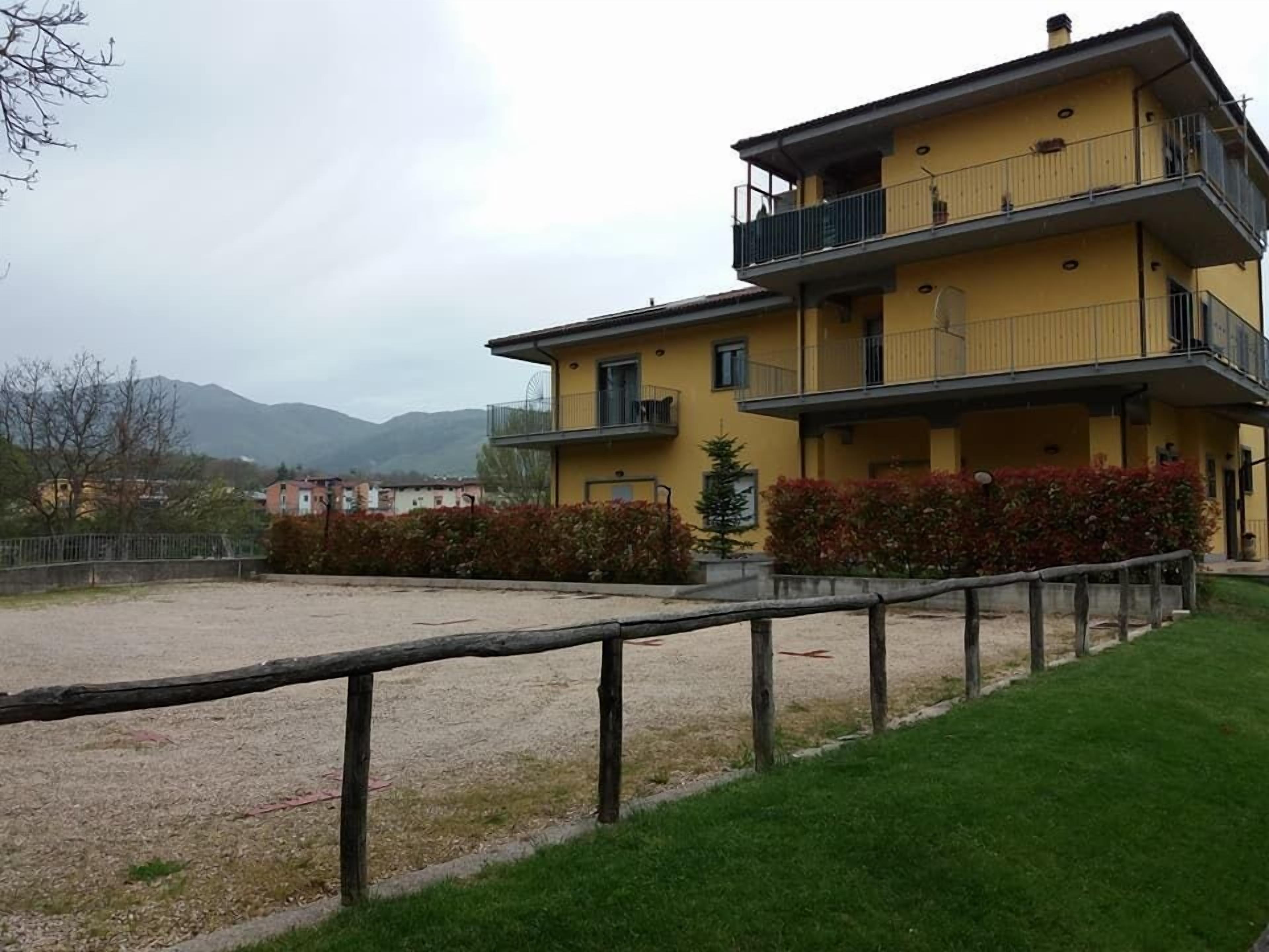 Un edificio amarillo de varios pisos con balcones, un área de grava al frente y un césped.