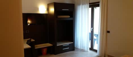 A hotel room with a bed, a desk with a chair, a wardrobe, and a window with curtains.