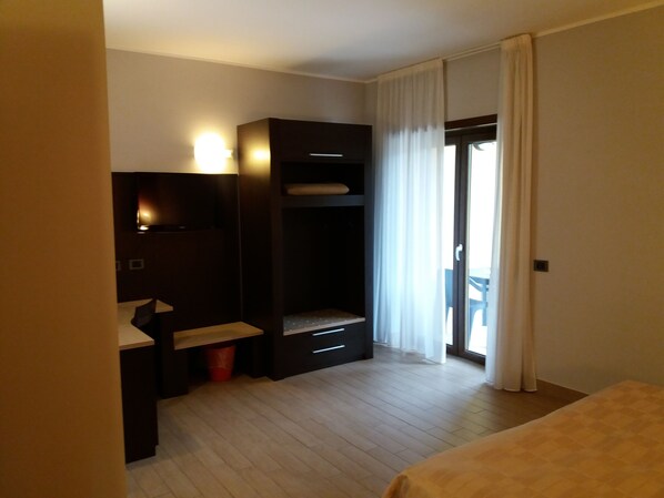 A hotel room with a bed, a desk with a chair, a wardrobe, and a window with curtains.