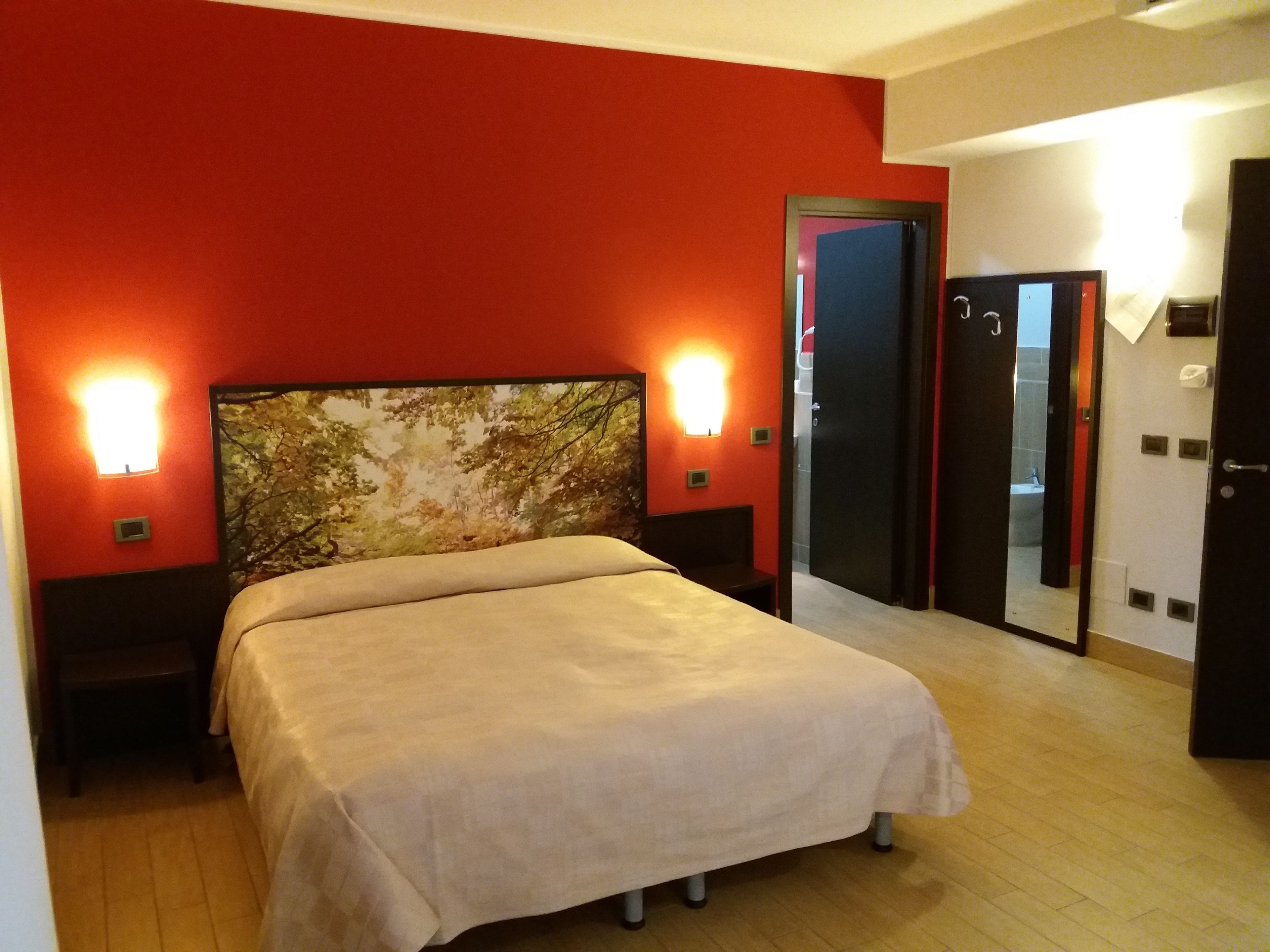 Habitación de hotel con cama, mesita de noche, lámpara de pared y puerta que da a un baño.