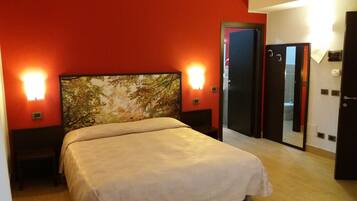 Habitación de hotel con cama, mesita de noche, lámpara de pared y puerta que da a un baño.