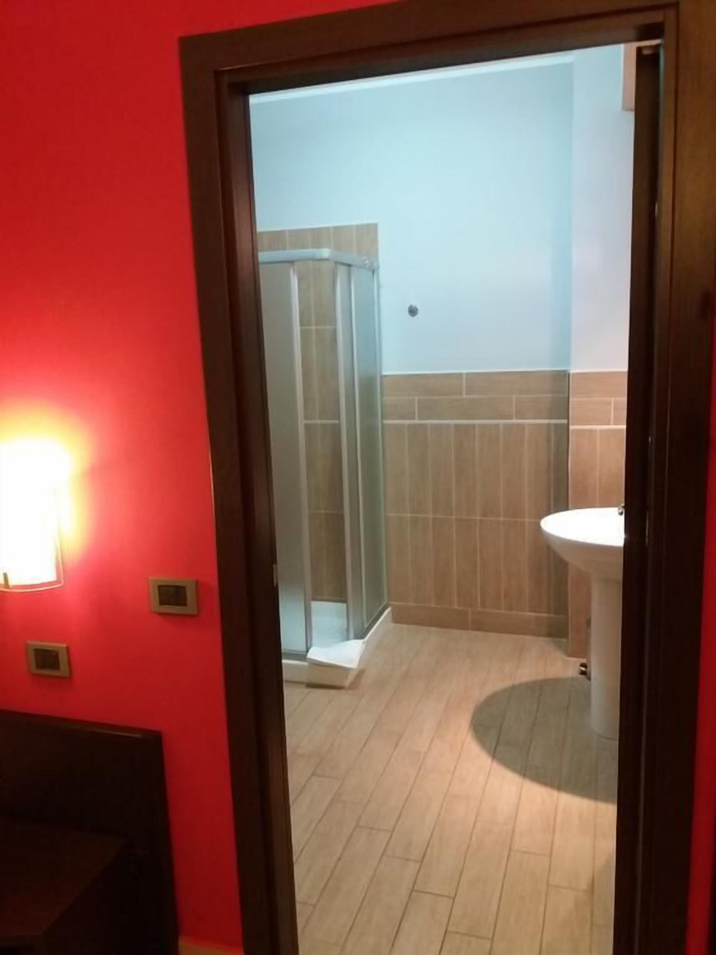 Un baño con cabina de ducha de vidrio, un lavamanos blanco y una pared roja.
