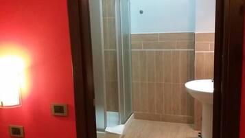 Un baño con cabina de ducha de vidrio, un lavamanos blanco y una pared roja.