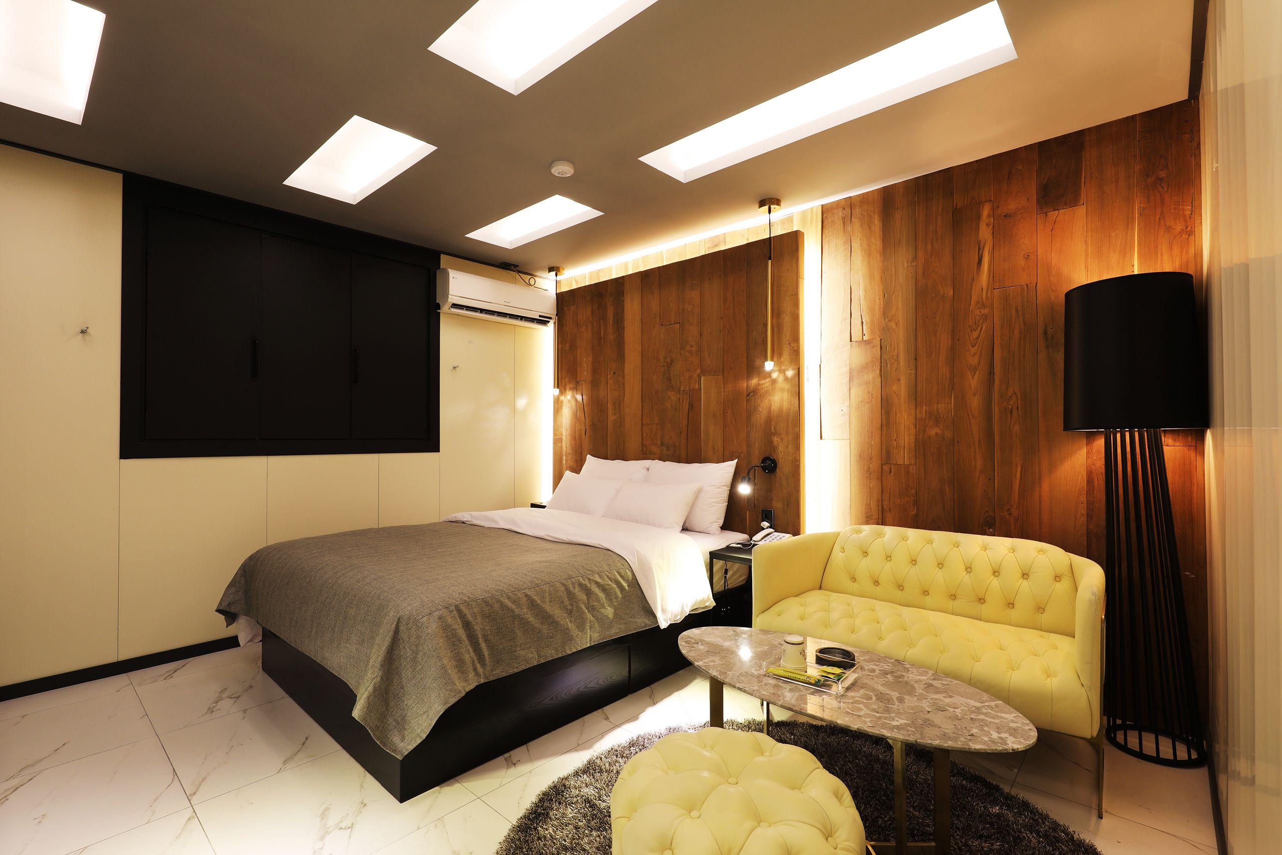 Een moderne slaapkamer met een bed, een gele slaapbank, een bijzettafeltje en een vloerlamp.