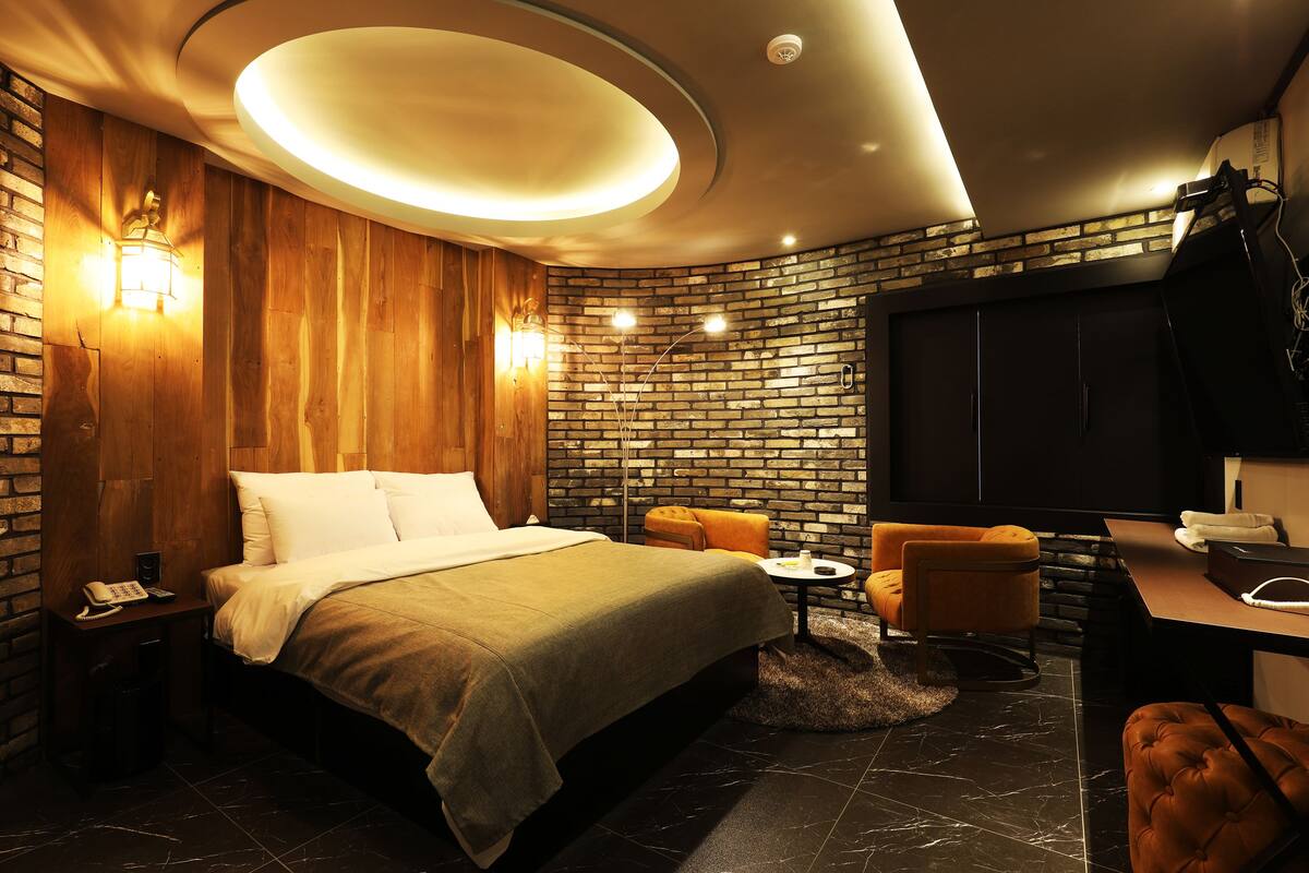 Una habitación de hotel moderna con pared de ladrillo, una cama grande, un escritorio y una zona de estar.