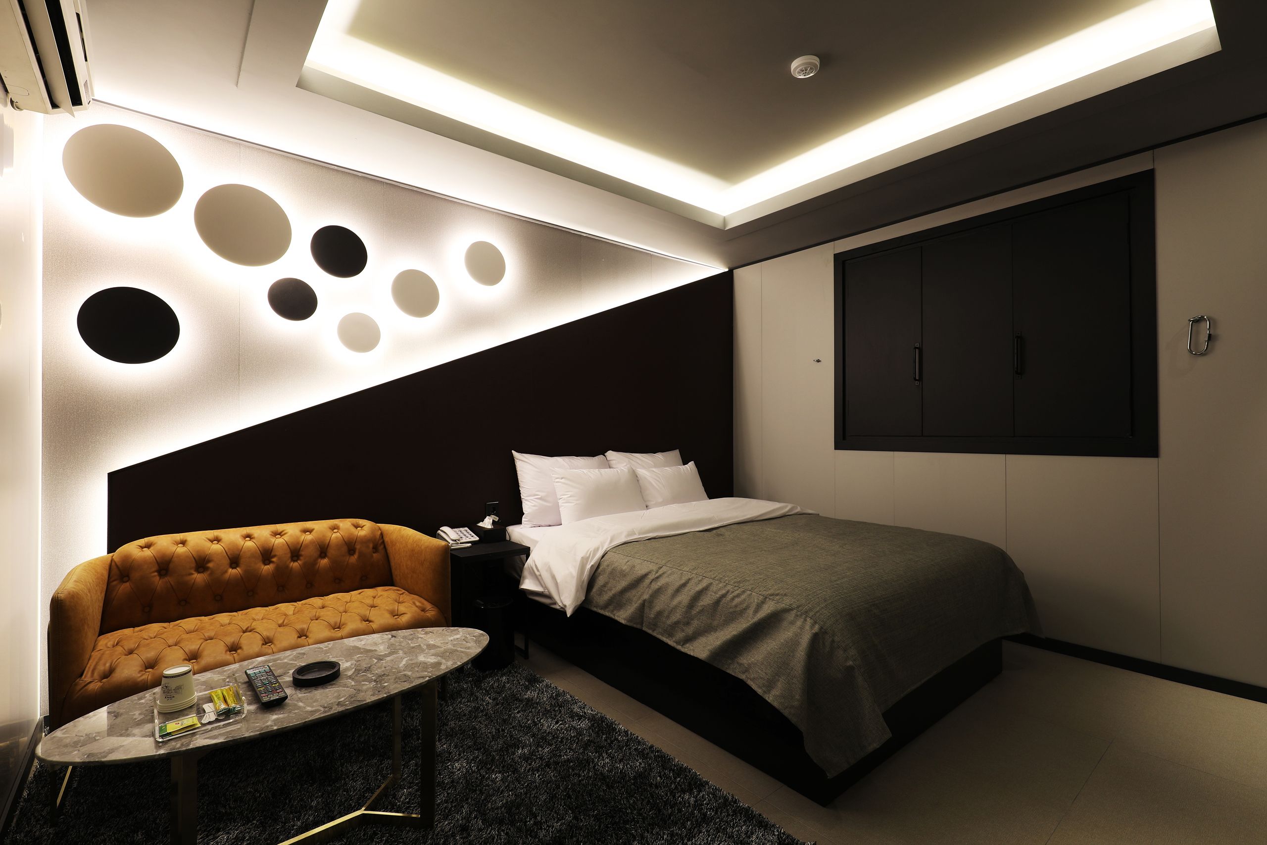 A modern hotel room with a sofa, a bed, a small table, and a wall with circular light fixtures.