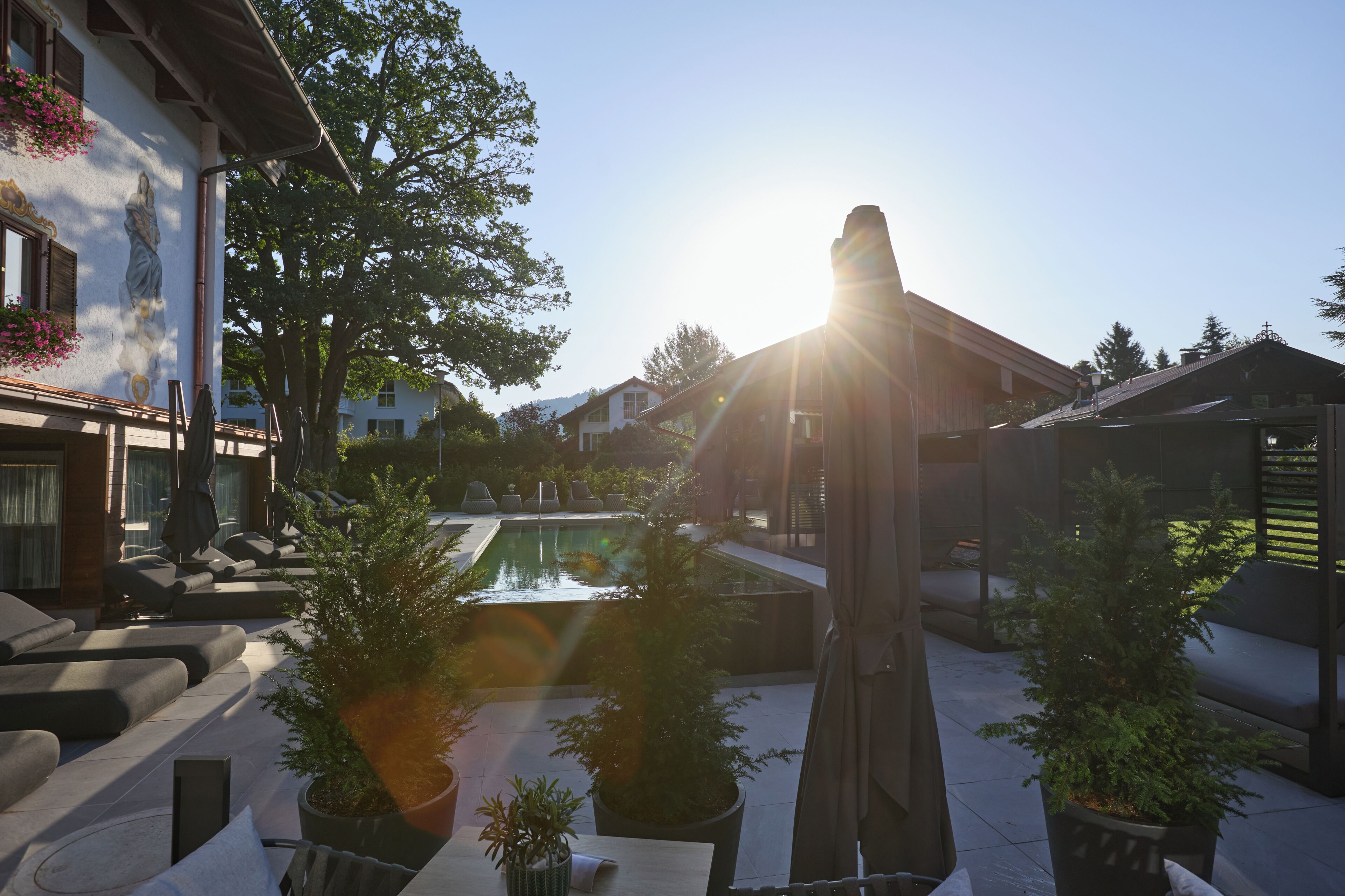 A courtyard with a pool, potted plants, outdoor furniture, and a building with a statue.