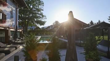 A courtyard with a pool, potted plants, outdoor furniture, and a building with a statue.